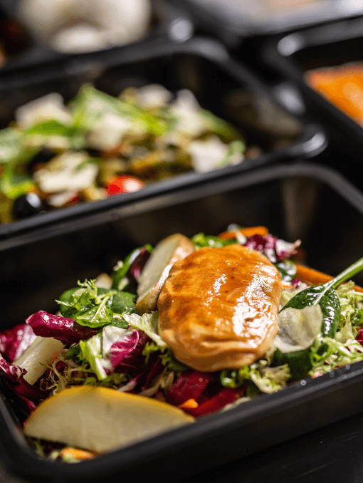 Closeup view of a prepared salad topped with glazed chicken in a black container