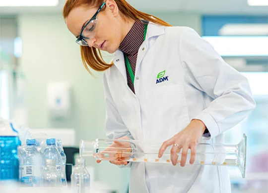 A scientist in a lab setting pouring liquid into clear container