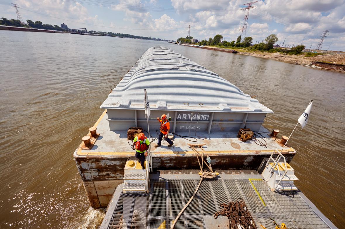 Two male deckhand workers wearing safety gear walking on barge in Mississippi River.