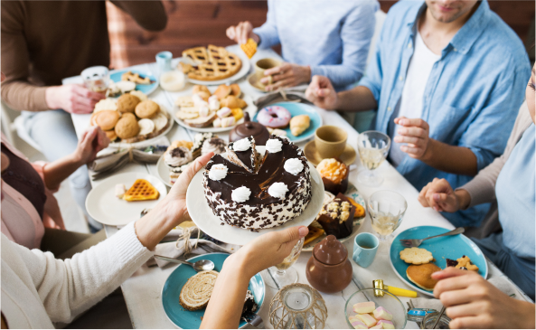 A group of friends sit around a table piled high with sugar reduced desserts passing plates amongst each other.