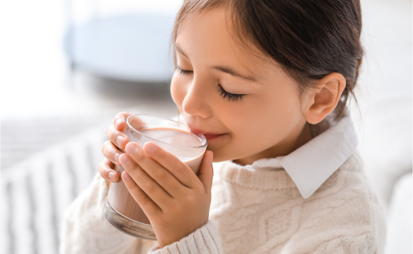 A young girl sips a reduced sugar milk drink from a glass.