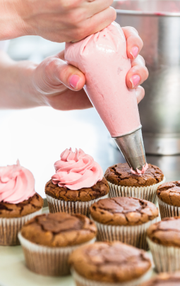 Someone using an icing bag to add reduced sugar pink icing to reduced sugar chocolate cupcakes arranged on a plate.