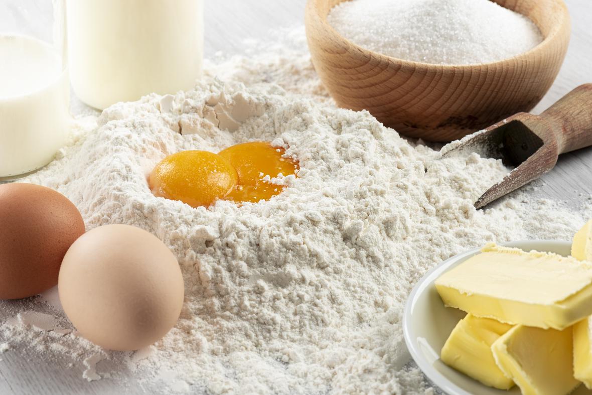 Two eggs cracked in a hill of flour surrounded by other baking ingredients