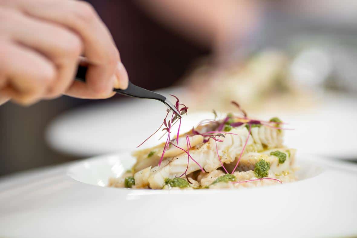 A chef carefully placing purple sprouts on cooked white fish