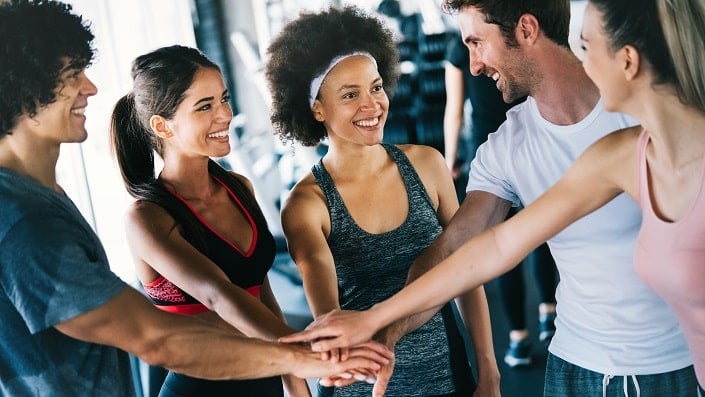 A group of diverse friends in gym clothes puts their hand together