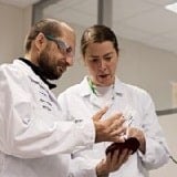 Two scientists in white coat are performing analysis and talking in a lab