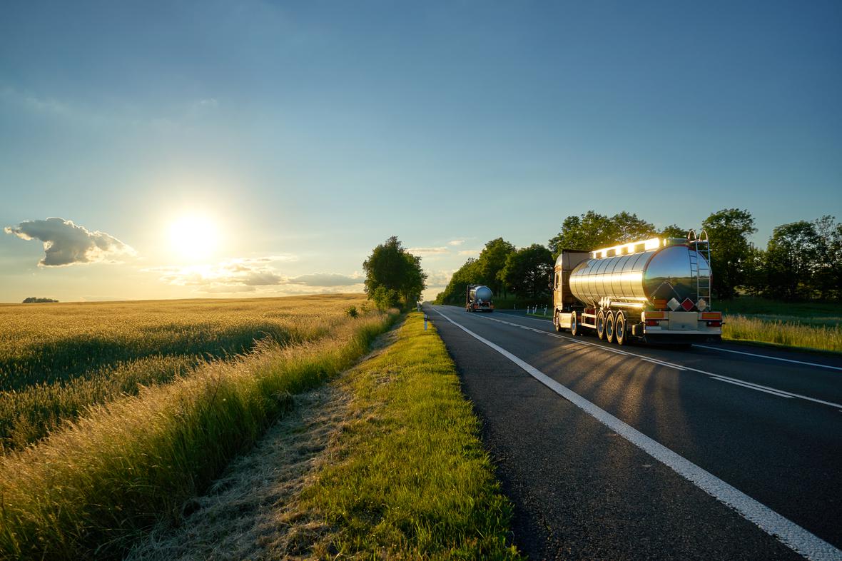 Chrome tanker trucks driving beside a field at sunrise